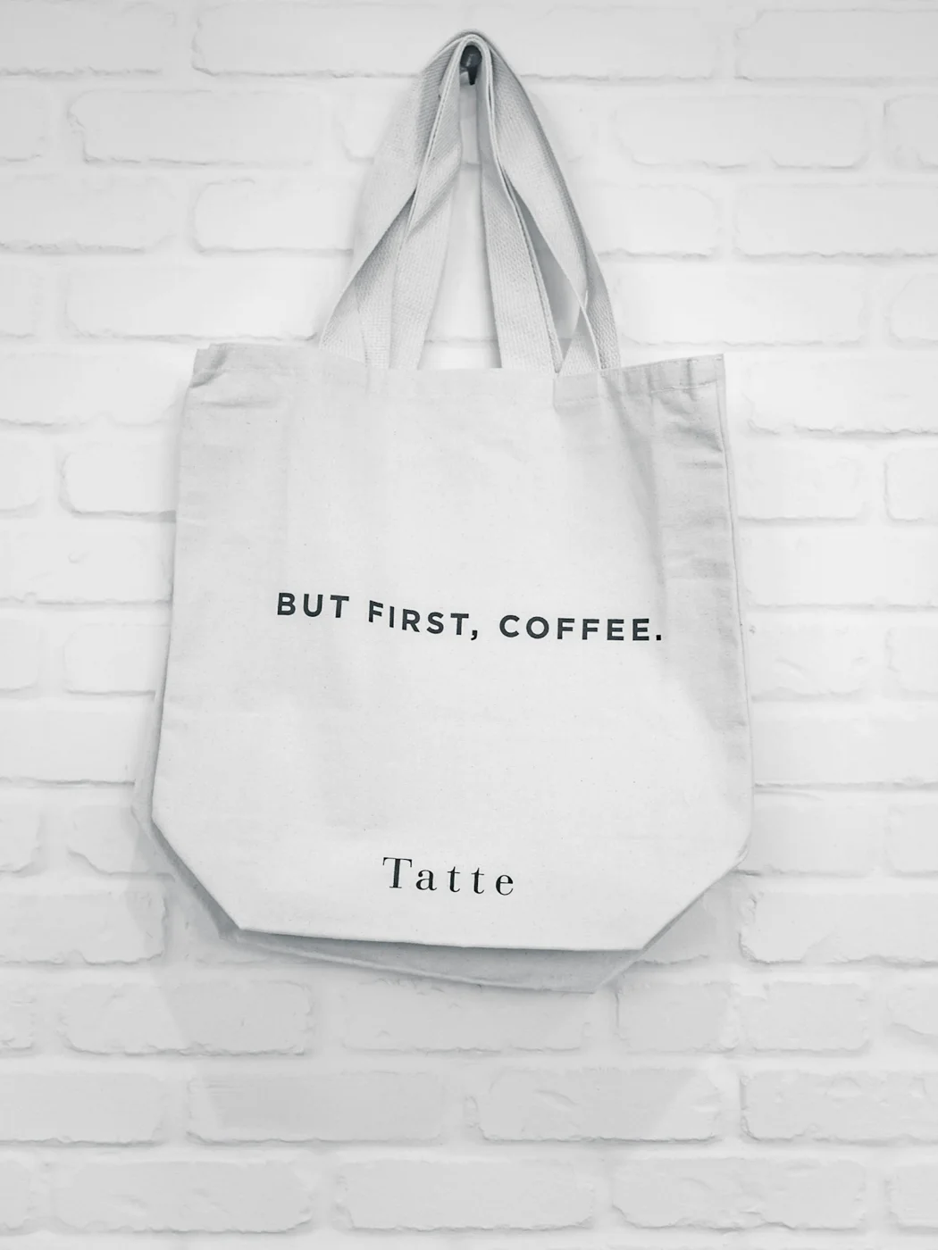 A white canvas tote bag hanging against a brick wall